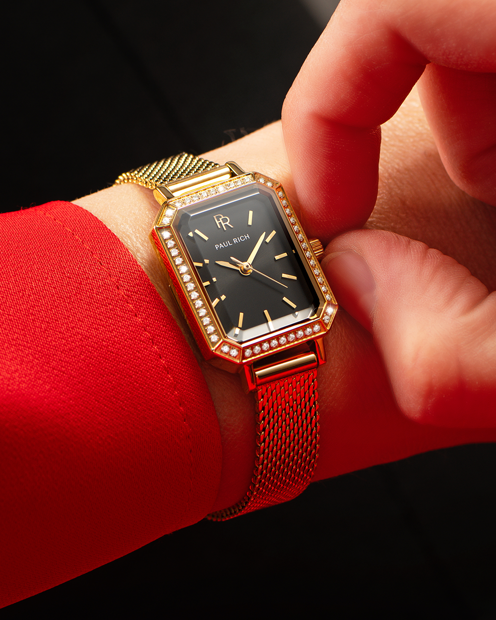 Gold watch with black face on a wrist against a red sleeve.